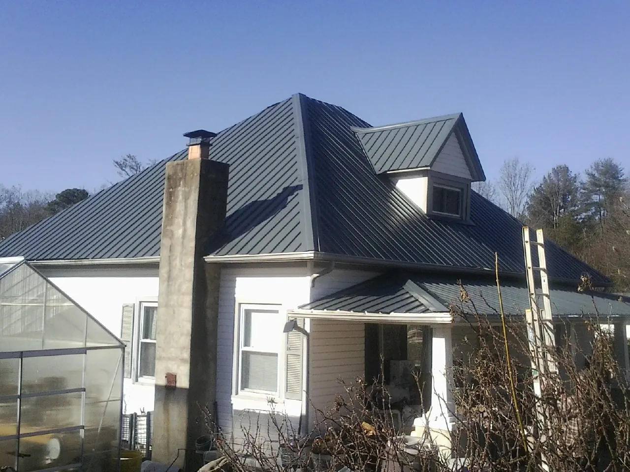 Dark blue standing seam metal roof on a white farmhouse with dormer — Slate & Tile Roof Repair by Roofing Brothers in Newdale