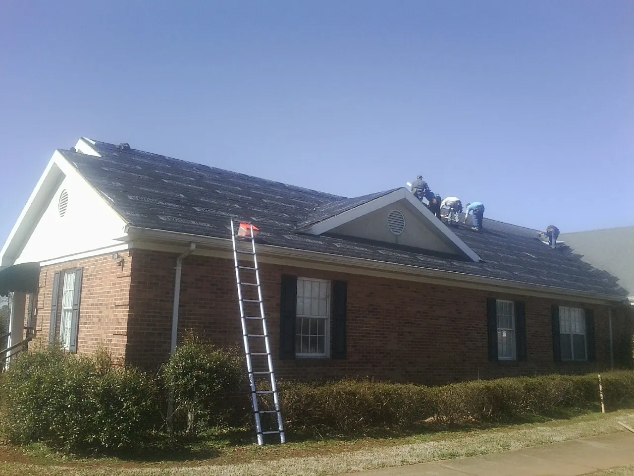 Crew tearing shingles off a brick ranch roof with a ladder set — Emergency Roof Repair work by our crew in Newdale
