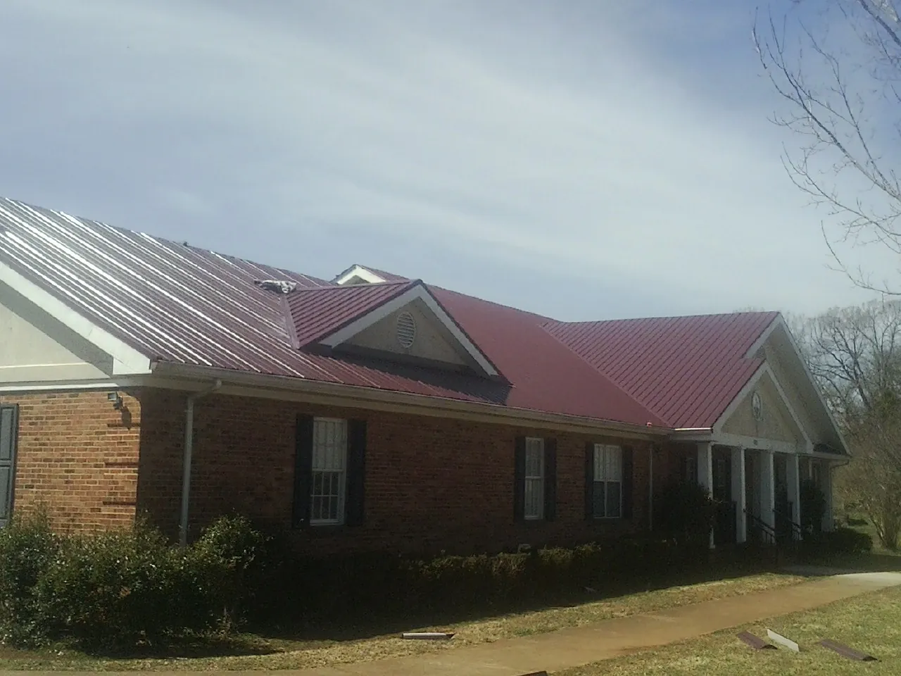 Red metal roof with gabled entries on a long brick building, from a Hail Damage Roof Repair job in Newdale