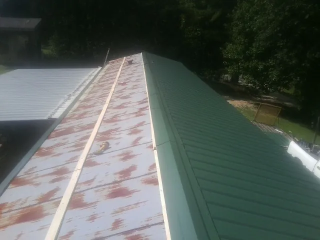 Old rusted panels beside newly installed green metal roofing — Wind Damage Roof Repair by Roofing Brothers in Newdale