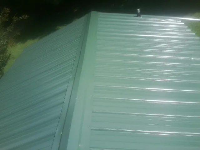 New green metal panels meeting at the ridge of a roof — Flat Roof Repair work by our crew in Newdale
