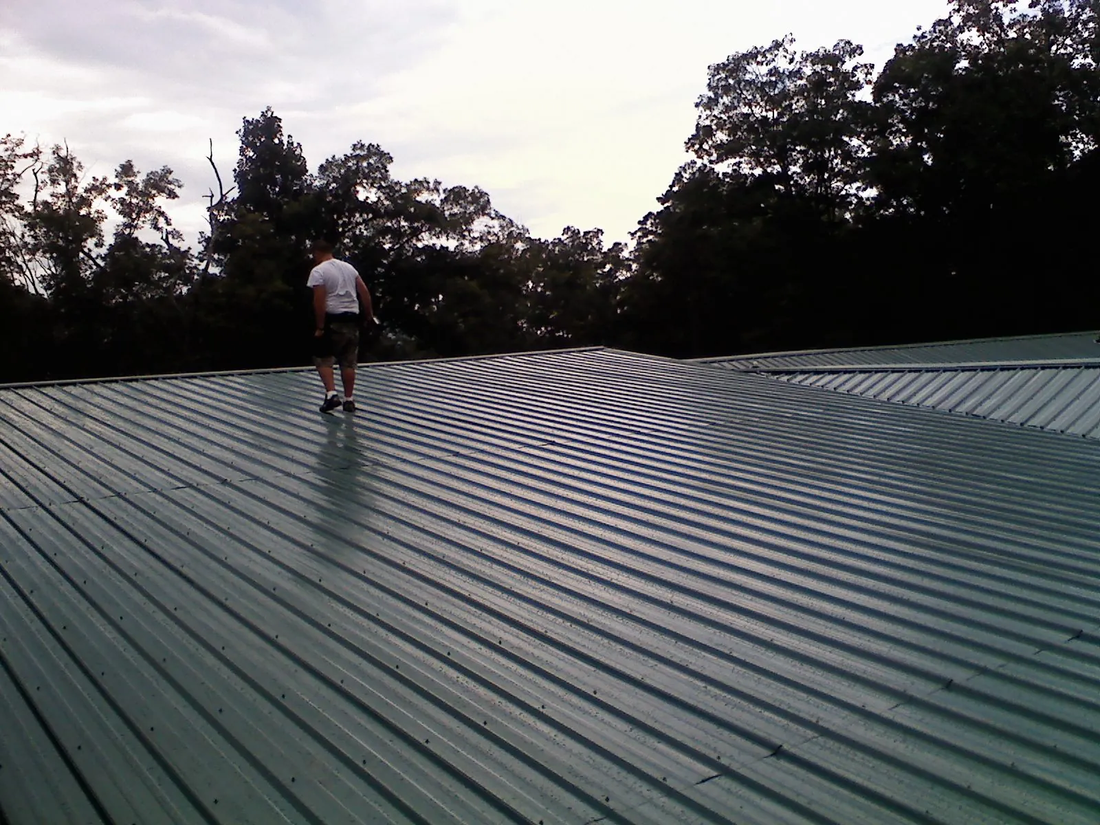 Roofer walking a wide expanse of new green metal roofing in Newdale