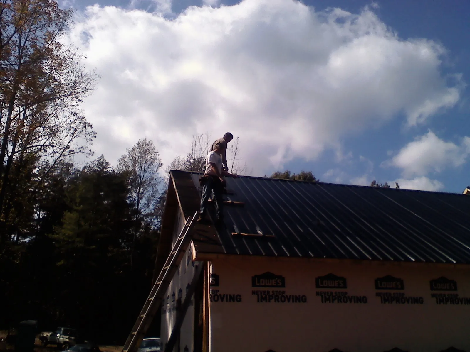 Roofer fastening dark metal panels high against a cloudy sky, from a Roof Inspection job in Newdale
