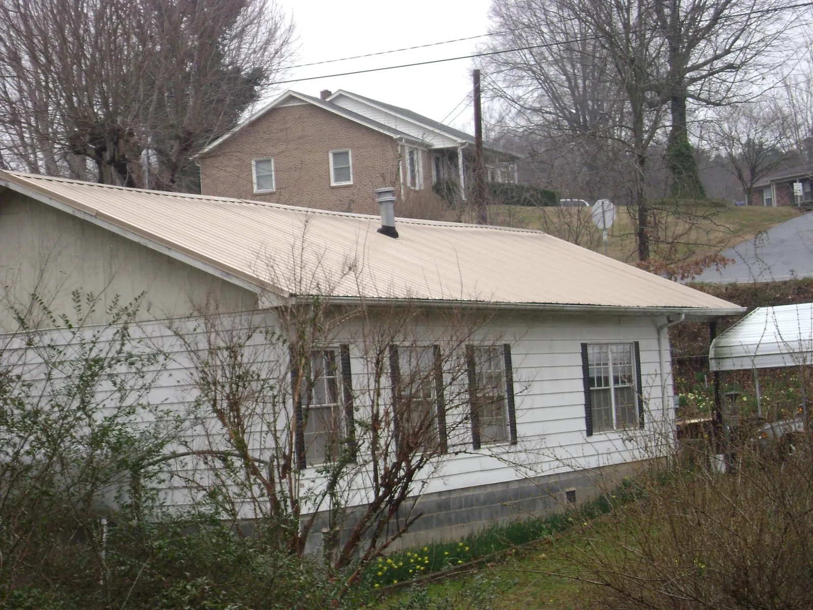 Tan metal roof on a white sided house set into a hillside — Commercial Roofing by Roofing Brothers in Newdale