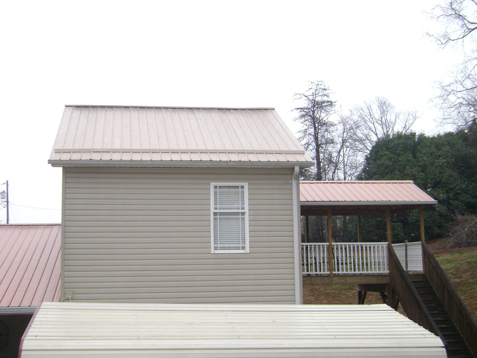 Tan metal roofs on a two story addition and attached porch, from a Roof Replacement job in Newdale